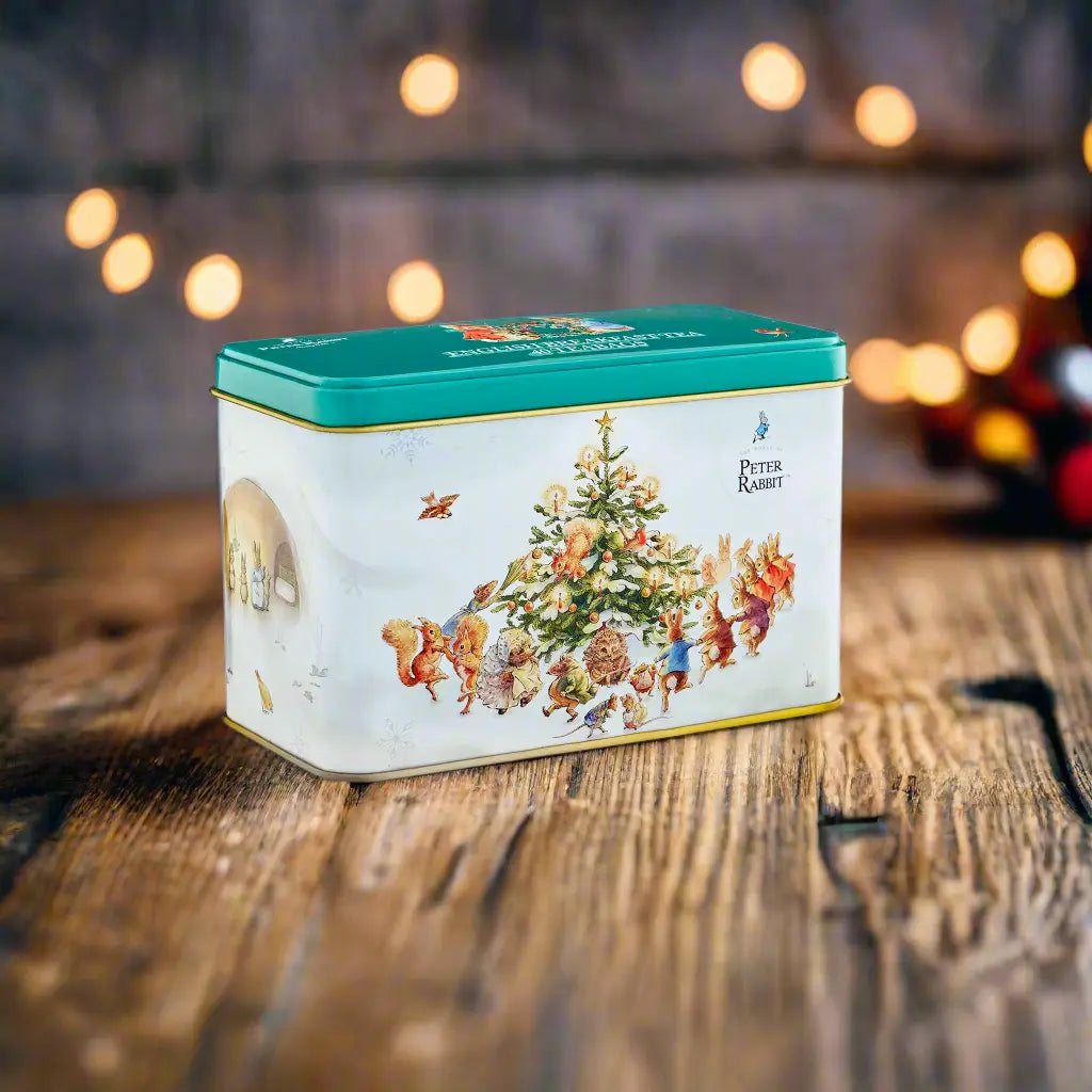 Decorative tea tin with a Peter Rabbit Christmas-themed design on a wooden surface with blurred lights in the background