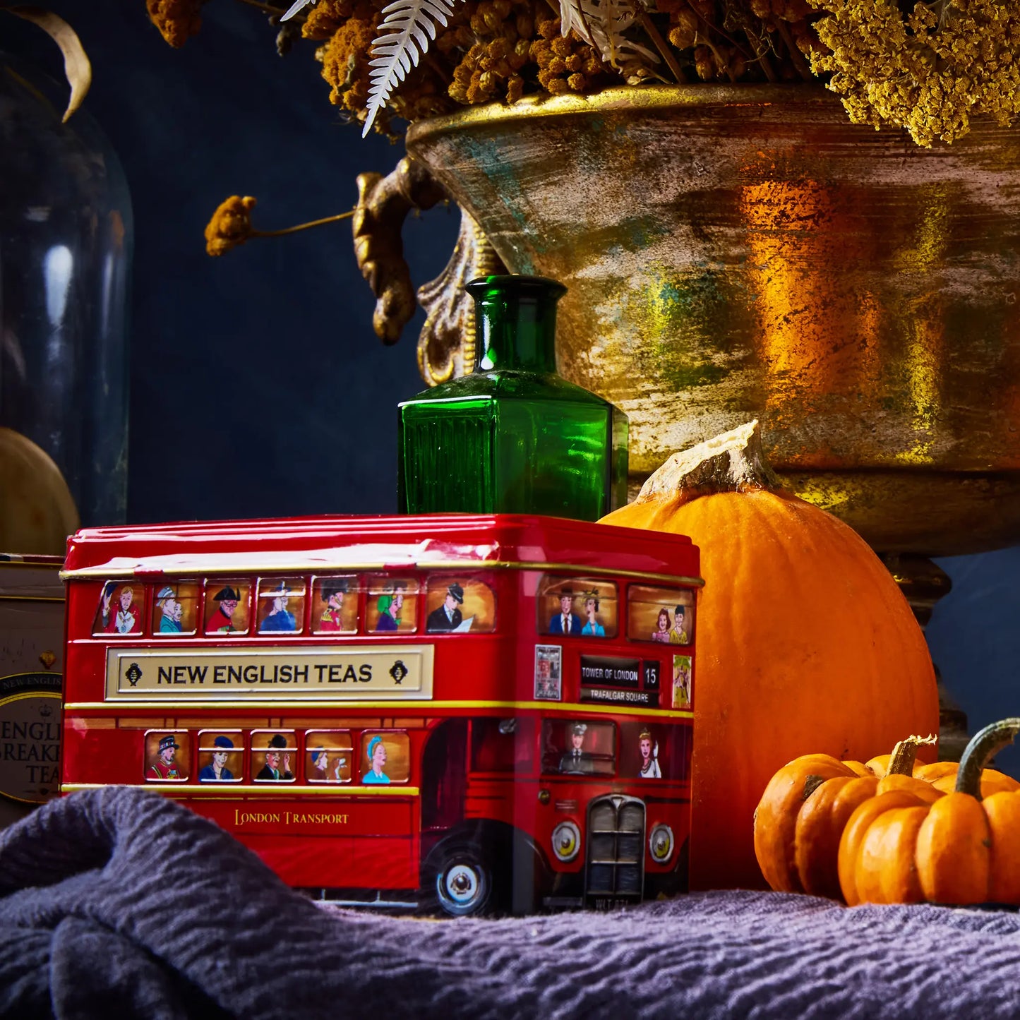 Red double-decker London bus tea box with pumpkins and a green bottle on a table top