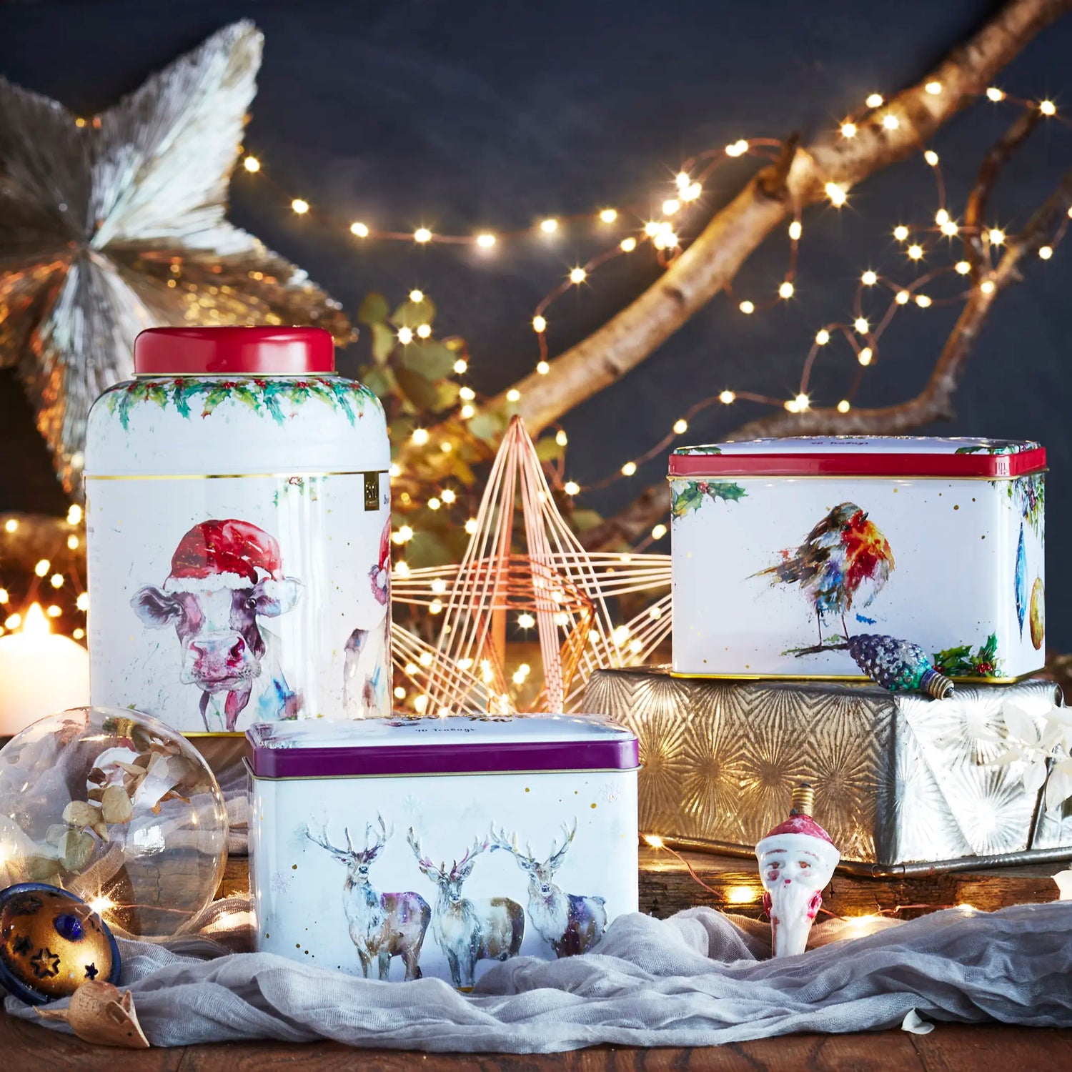 Three decorative tea tins with animal illustrations on a festive background with lights and ornaments.