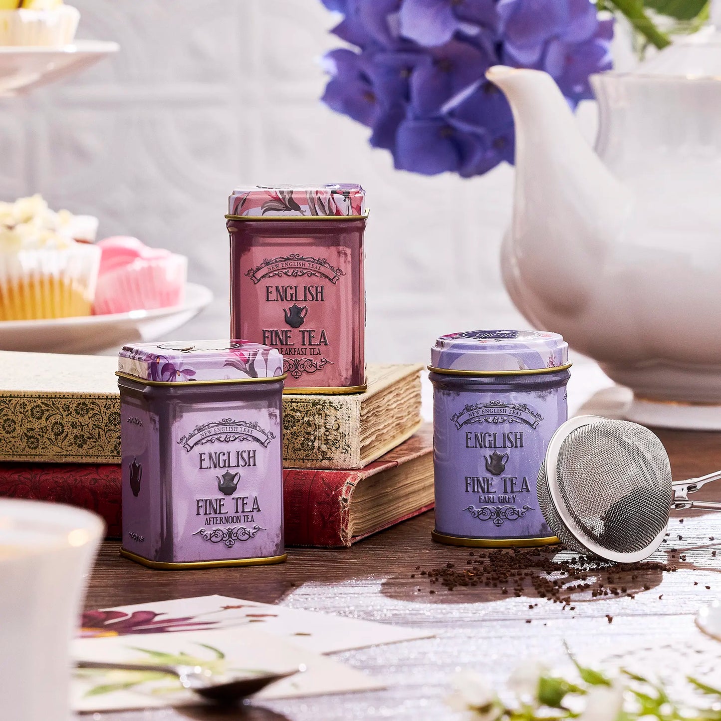 Tea tins with 'English Fine Tea' branding on a table with a teapot and books in the background.