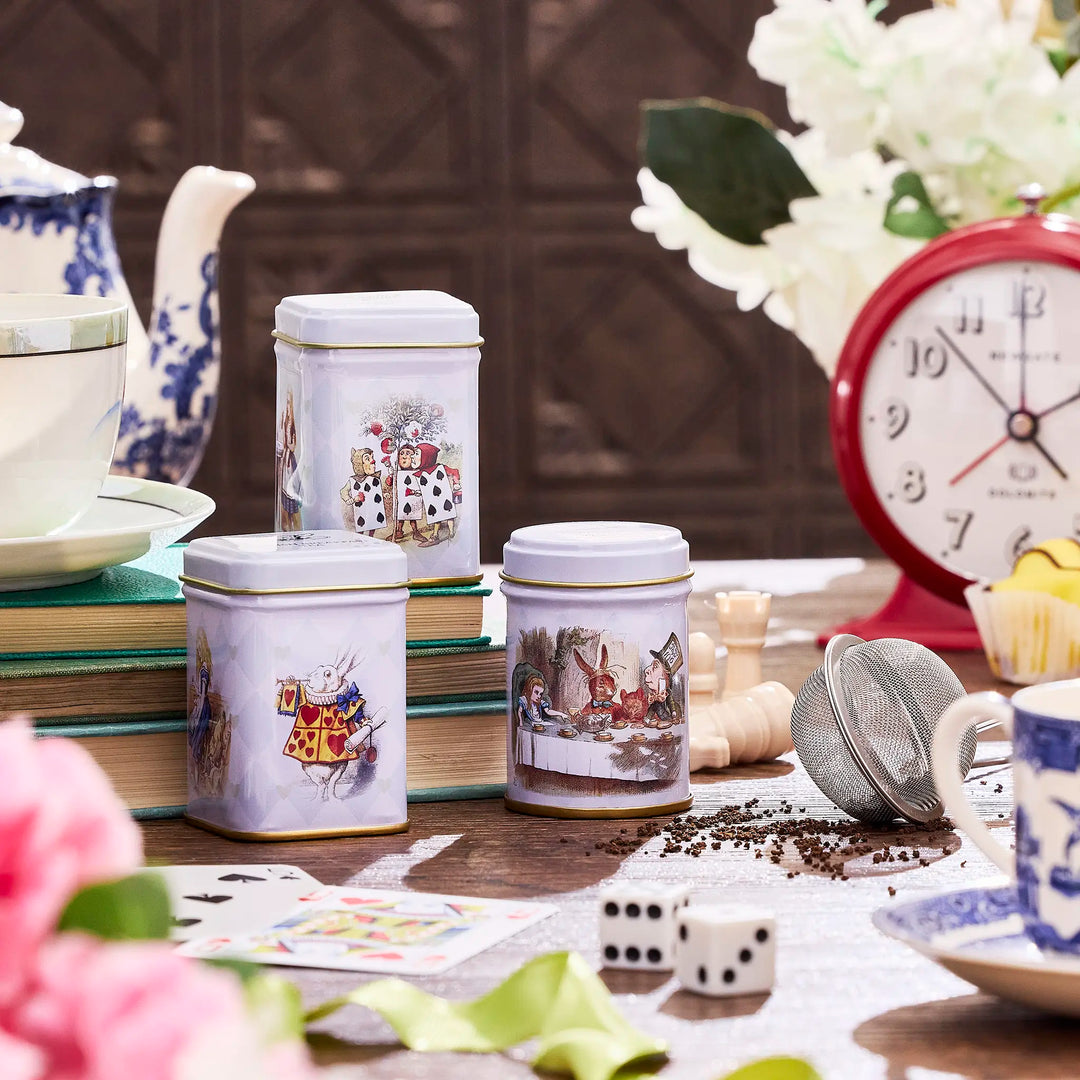 Tea canisters with illustrations on a table with books and flowers