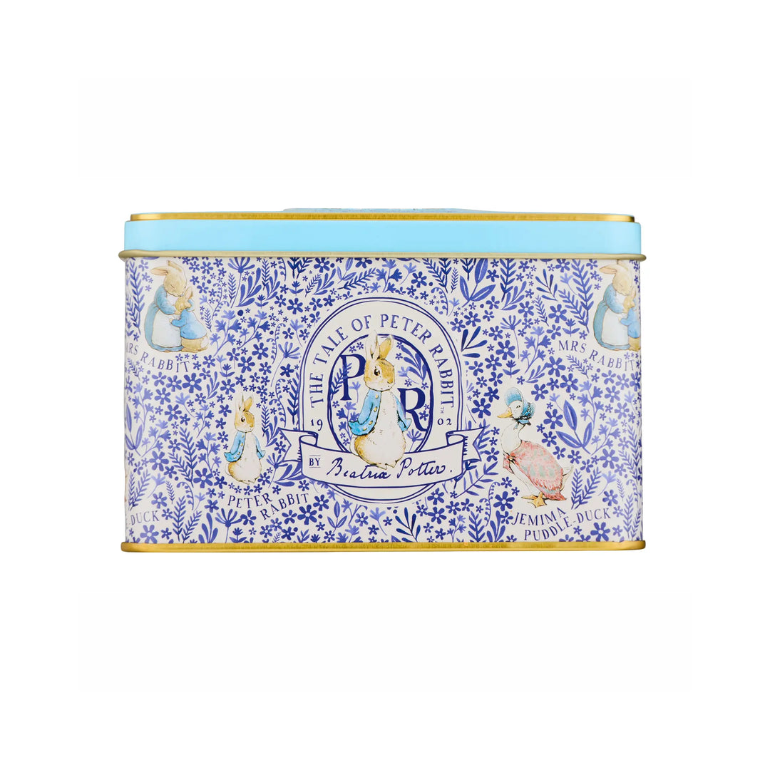 A rectangular metal tin with a light blue lid and gold trim, decorated with a blue floral pattern and illustrations from Peter Rabbit, including Beatrix, Peter Rabbit, and the title 'The Time of Peter Rabbit'.