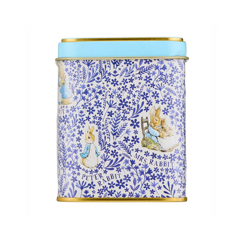 A cylindrical metal tin with a blue and white floral pattern featuring Peter Rabbit and Mrs. Rabbit illustrations, topped with a light blue lid and finished with gold-toned metal rims.