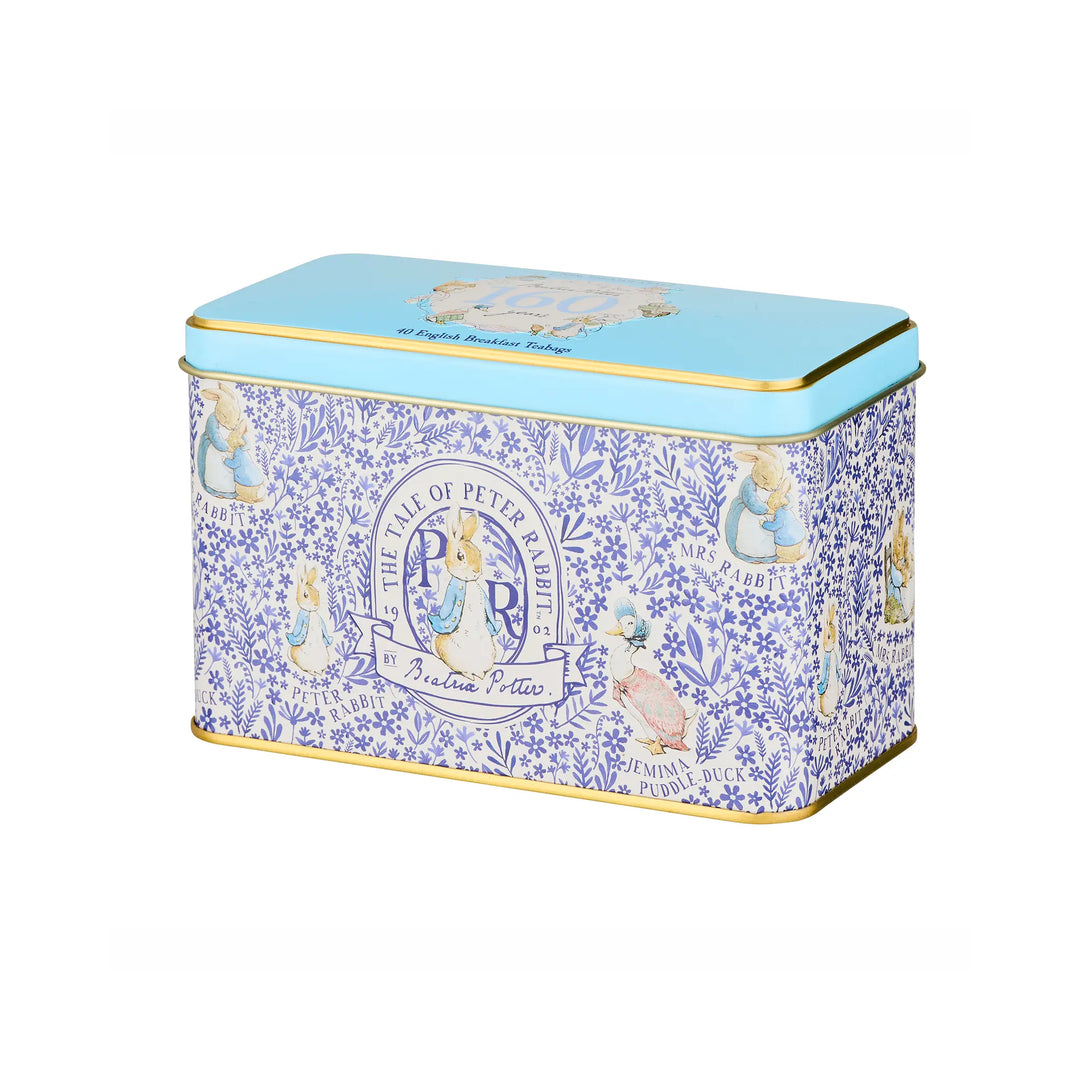 A rectangular metal tin with a light blue lid and gold trim, decorated with a blue floral pattern and Peter Pan illustrations on the sides, photographed on a plain white background.