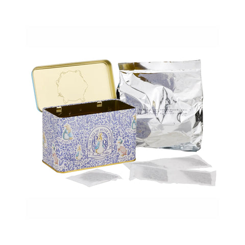 A decorative blue and white patterned metal tea tin with gold trim, shown open with a silver foil pouch and several tea bags on a white background.