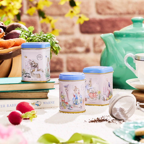 Tea canisters with illustrations on a table with a teapot and books in the background