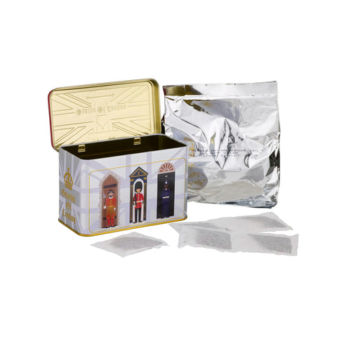 A tin of tea with an illustrated front panel showing three guards at doors, next to a silver foil pouch and several teabags on a white background.