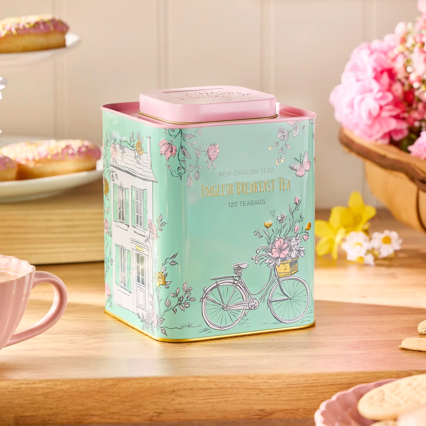 Tea tin with floral design on a wooden table with a cup and cookies.