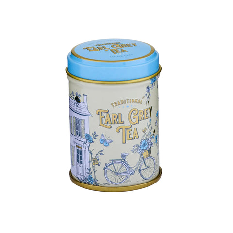 A cylindrical metal tea tin for Earl Grey Tea, featuring a cream-colored body with blue illustrations of a house, bicycle, and flowers, and a light blue lid with gold lettering.