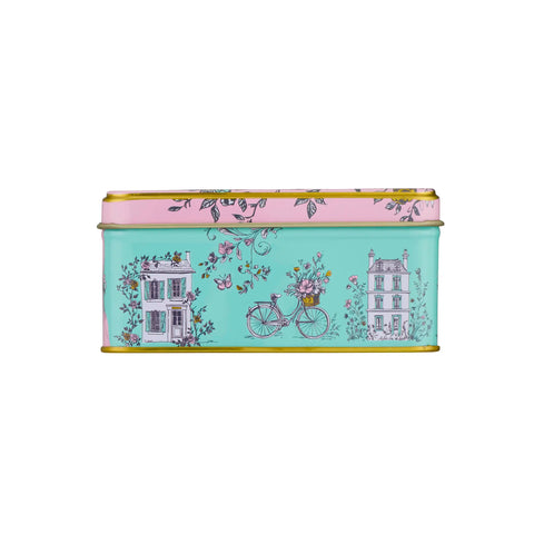 A rectangular metal tin with a light aqua background and a pink top band, decorated with a vintage-style illustration of a bicycle, flowers, and two houses. The tin has gold-toned metal edges and is shown against a plain white background.