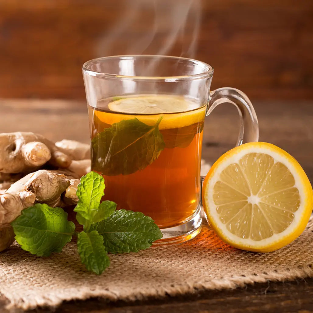 Glass mug of hot tea with lemon and ginger on a wooden surface