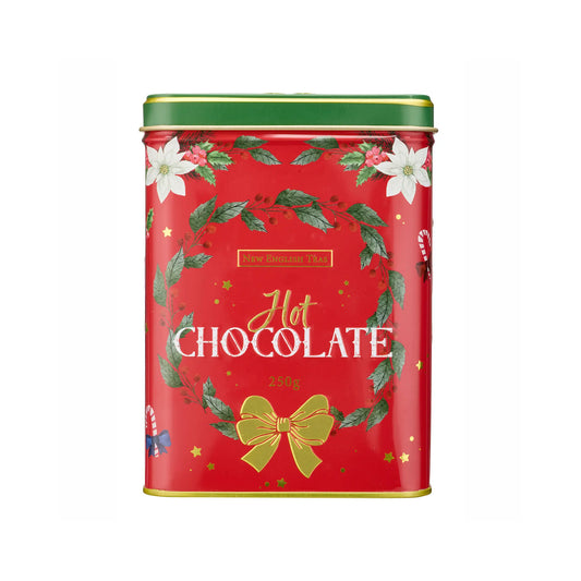 A red metal tin of Hot Chocolate with a green lid, decorated with green holly leaves, white poinsettias, a gold bow, and gold stars on a white background.