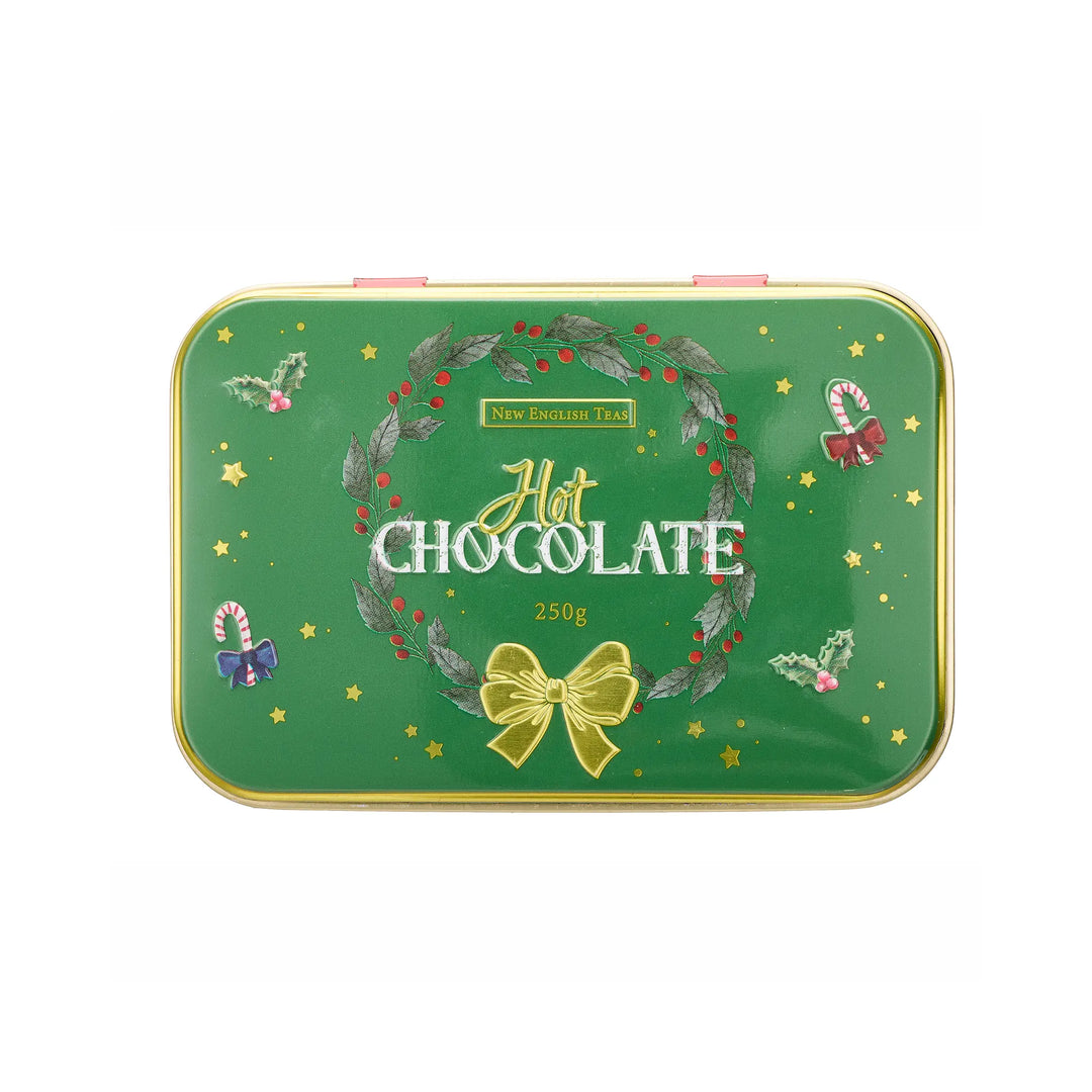A rectangular green tin lid of New English Teas Hot Chocolate, decorated with a festive wreath, gold bow, candy canes, and stars, shown on a plain white background.
