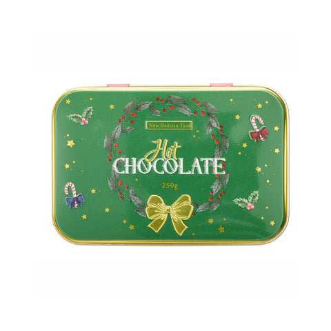 A rectangular green tin lid of New English Teas Hot Chocolate, decorated with a festive wreath, gold bow, candy canes, and stars, shown on a plain white background.