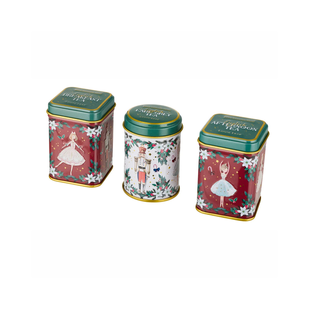 Three decorative metal tea tins with Christmas-themed illustrations, including a nutcracker and ballerina designs, on a plain white background.