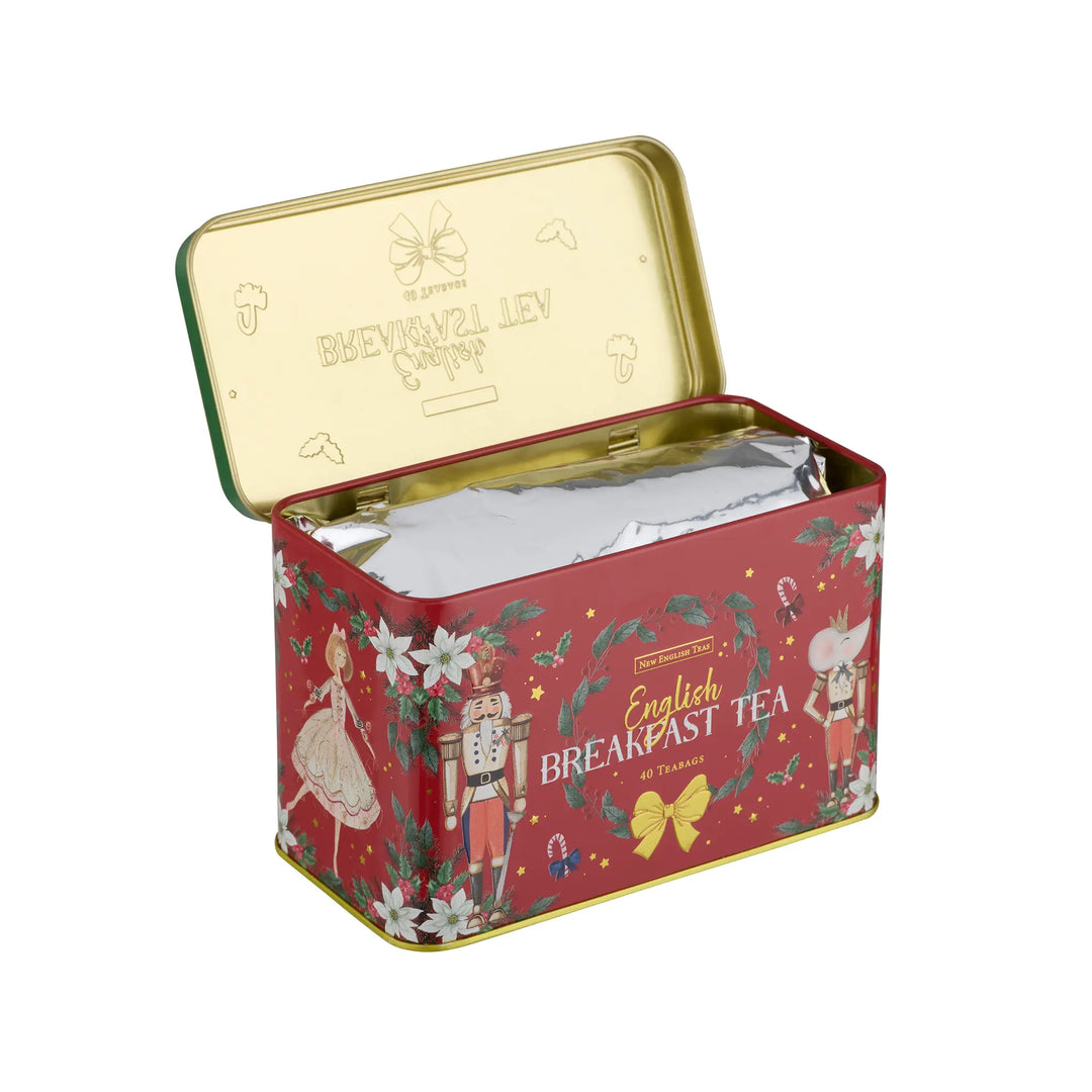 A red metal tin of English Breakfast Tea shown open to reveal silver foil packets inside. The tin features festive illustrations of a nutcracker, a mouse, and white flowers, with gold lettering and trim, set against a plain white background.