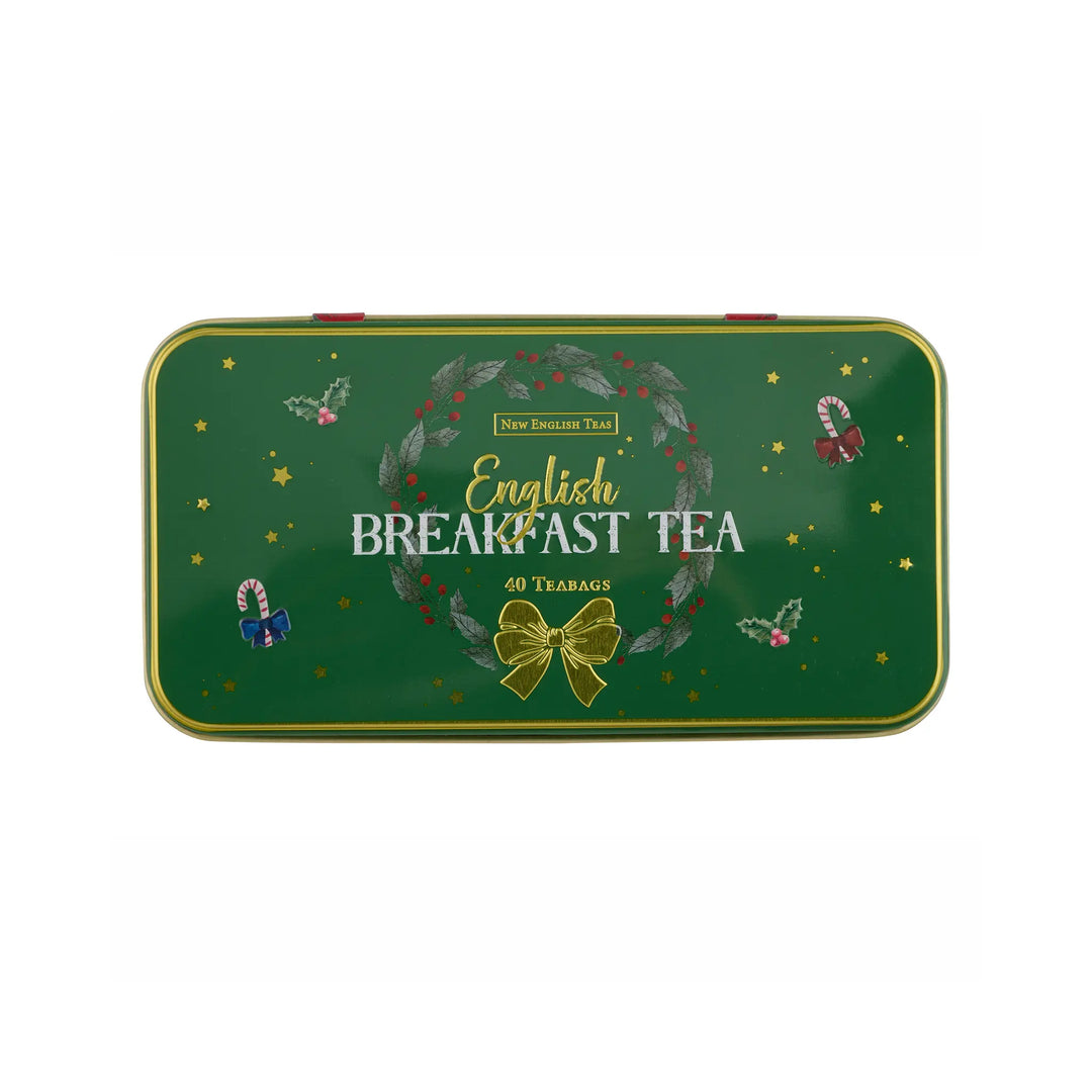 A rectangular green metal tin of New English Tea English Breakfast Tea, decorated with a wreath, gold bow, and festive illustrations, on a plain white background.