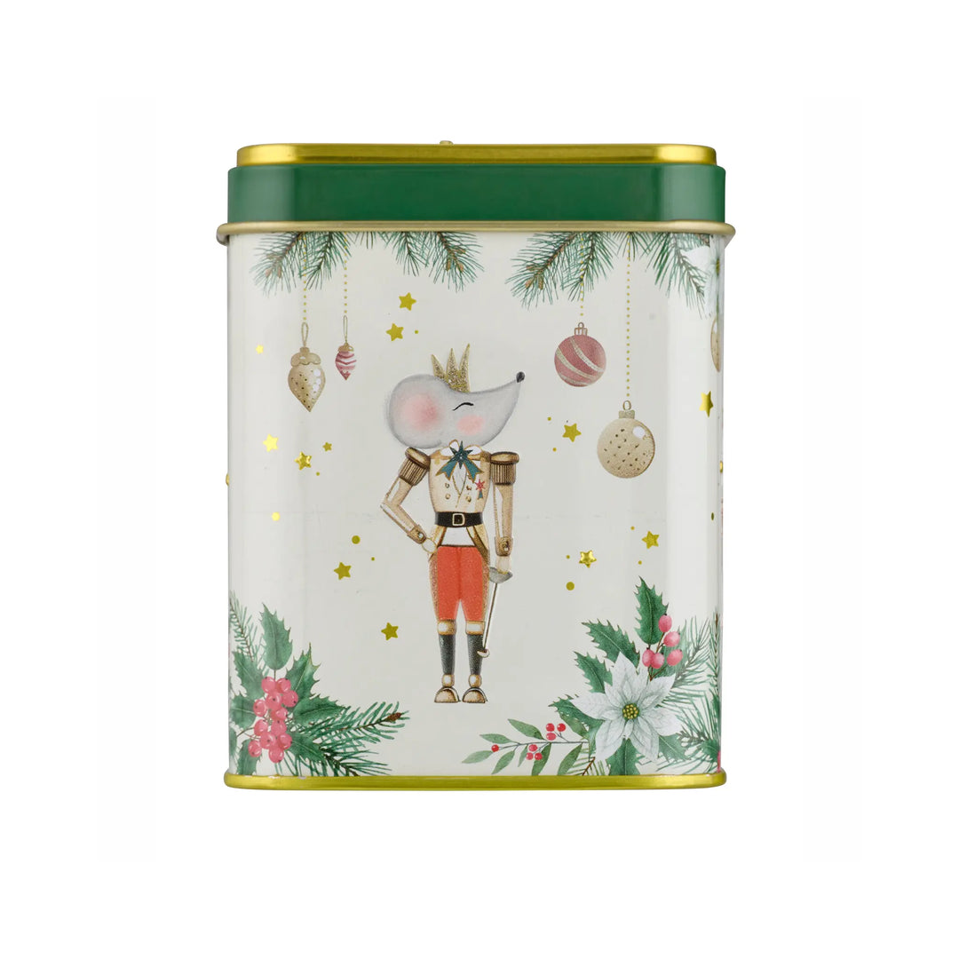 A cylindrical Christmas-themed tin with a white body, decorated with a nutcracker illustration, pine branches, ornaments, stars, and flowers. The tin has a dark green lid with gold trim and a gold-colored rim.