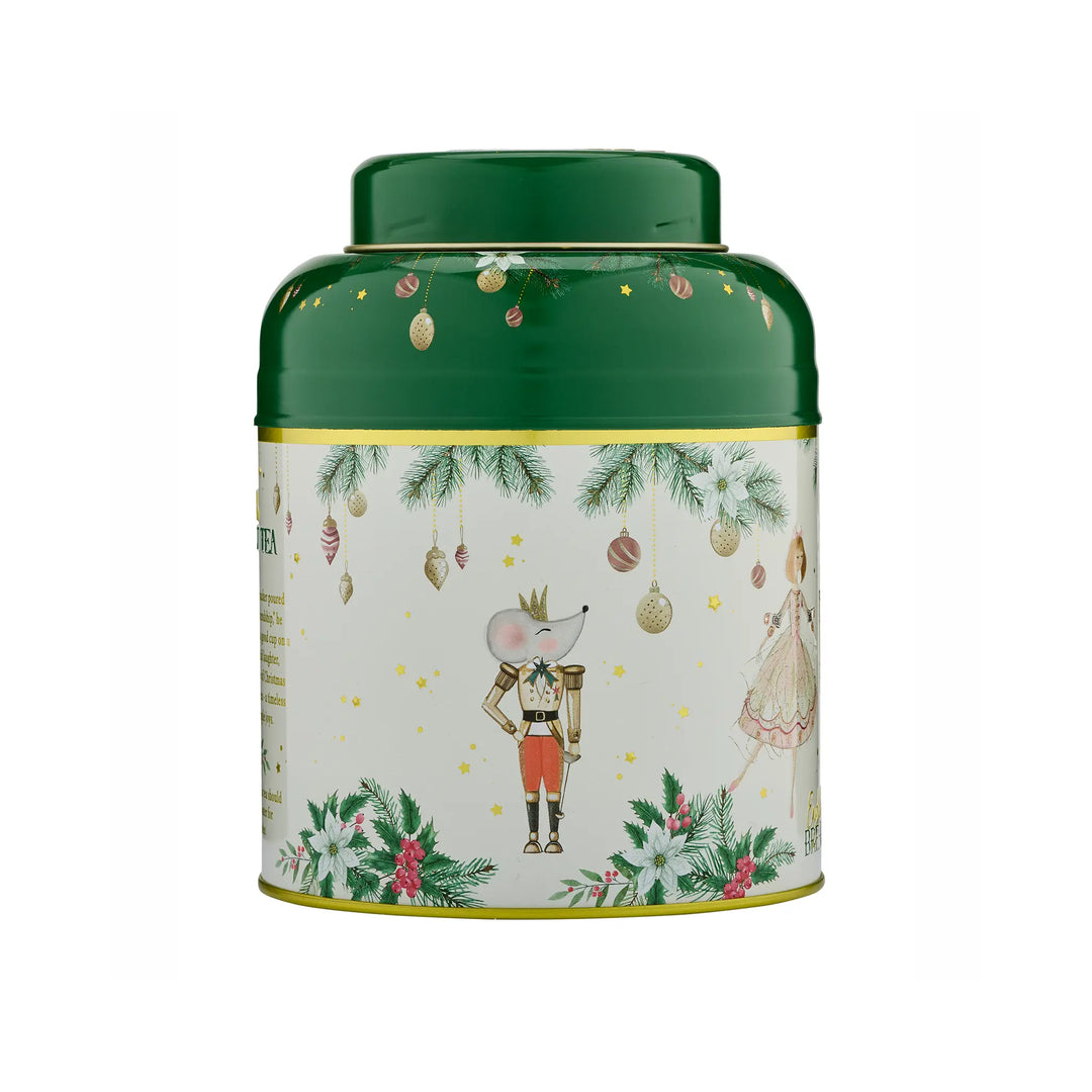 A cylindrical metal tea tin with a dark green lid and base, featuring a cream-coloured illustrated label with a nutcracker, a mouse in a dress, pine branches, ornaments, and small gold stars.