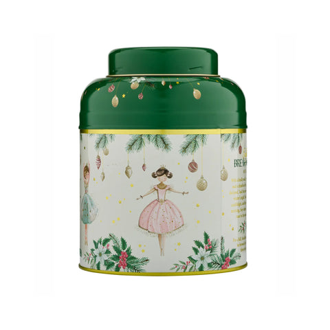 A round metal tea tin with a dark green lid and a cream-colored label decorated with Christmas illustrations, including a ballerina in a pink dress, hanging ornaments, pine branches, and festive greenery.