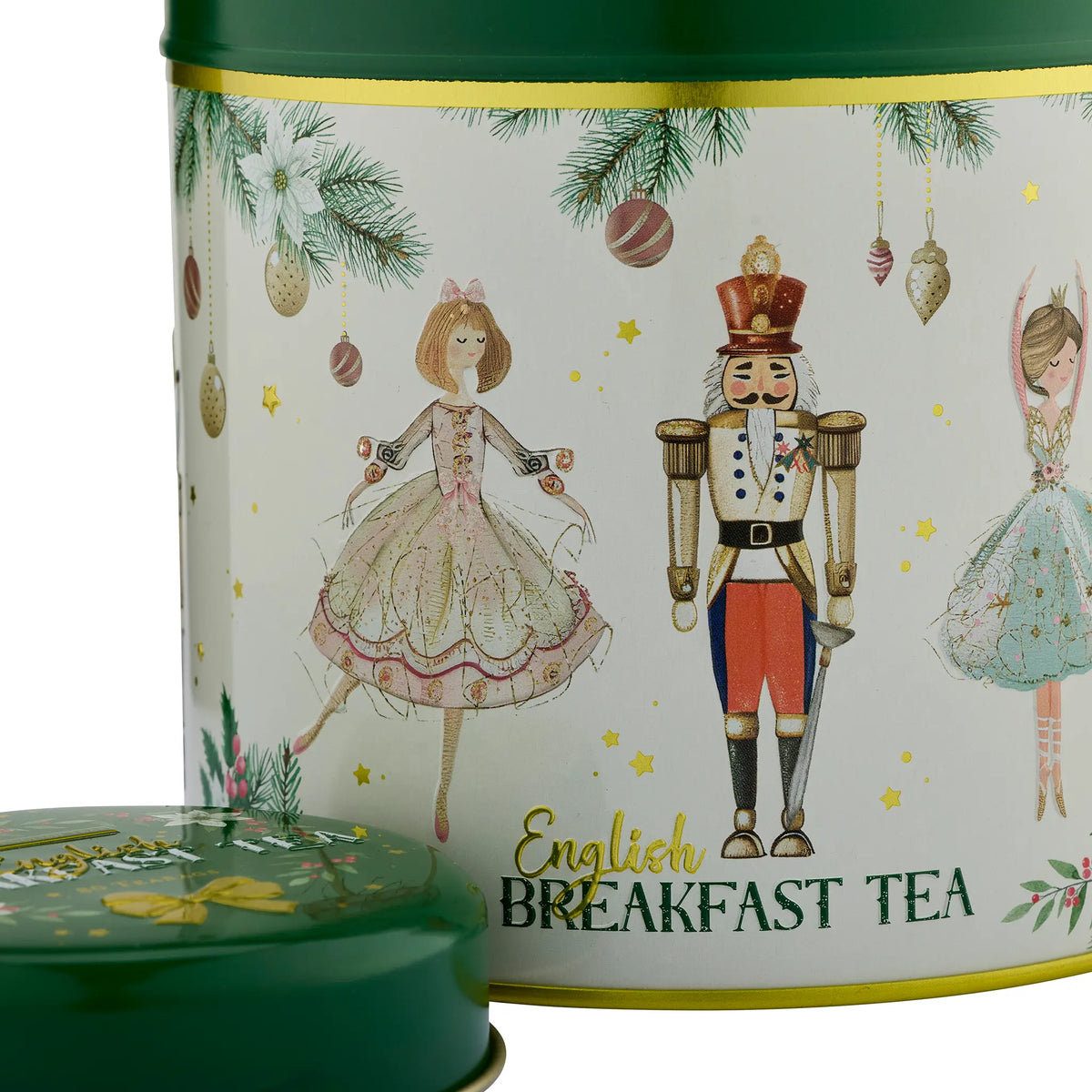 A cylindrical tin of English Breakfast Tea with a dark green lid partially visible in the foreground. The tea tin features a white label decorated with Christmas illustrations, including a nutcracker, ballerinas, pine branches, ornaments, and gold stars.