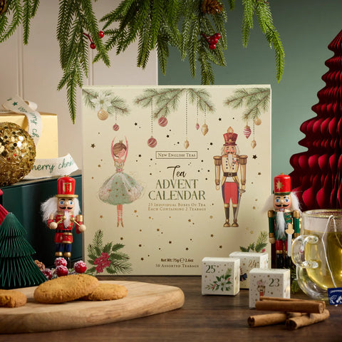 A Christmas-themed tea advent calendar box displayed on a tabletop with cookies, nutcrackers, tea, and holiday decorations around it. The front of the box reads 'New England Tea  Advent Calendar' and shows festive illustrations of a ballerina and a nutcracker.
