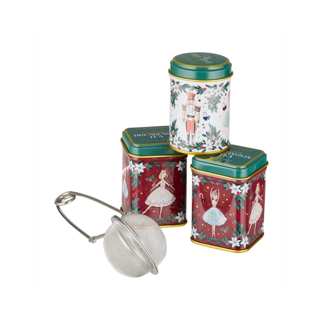 Three decorative metal tea tins with a silver mesh tea infuser, arranged on a plain white background. The tins feature festive holiday illustrations including ballerinas, a nutcracker, snowflakes, and green lids.