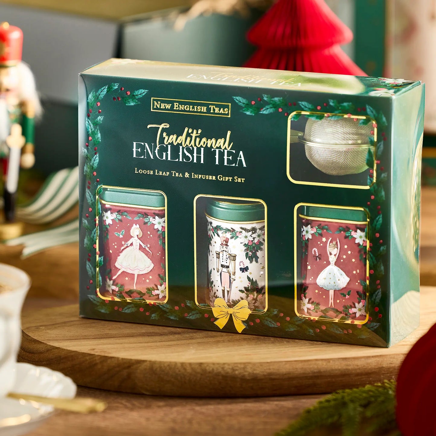 New English Tea Traditional English Tea Loose Leaf Tea & Infuser Gift Set in a dark green box with festive illustrations, displayed on a wooden tray in a holiday-themed setting.