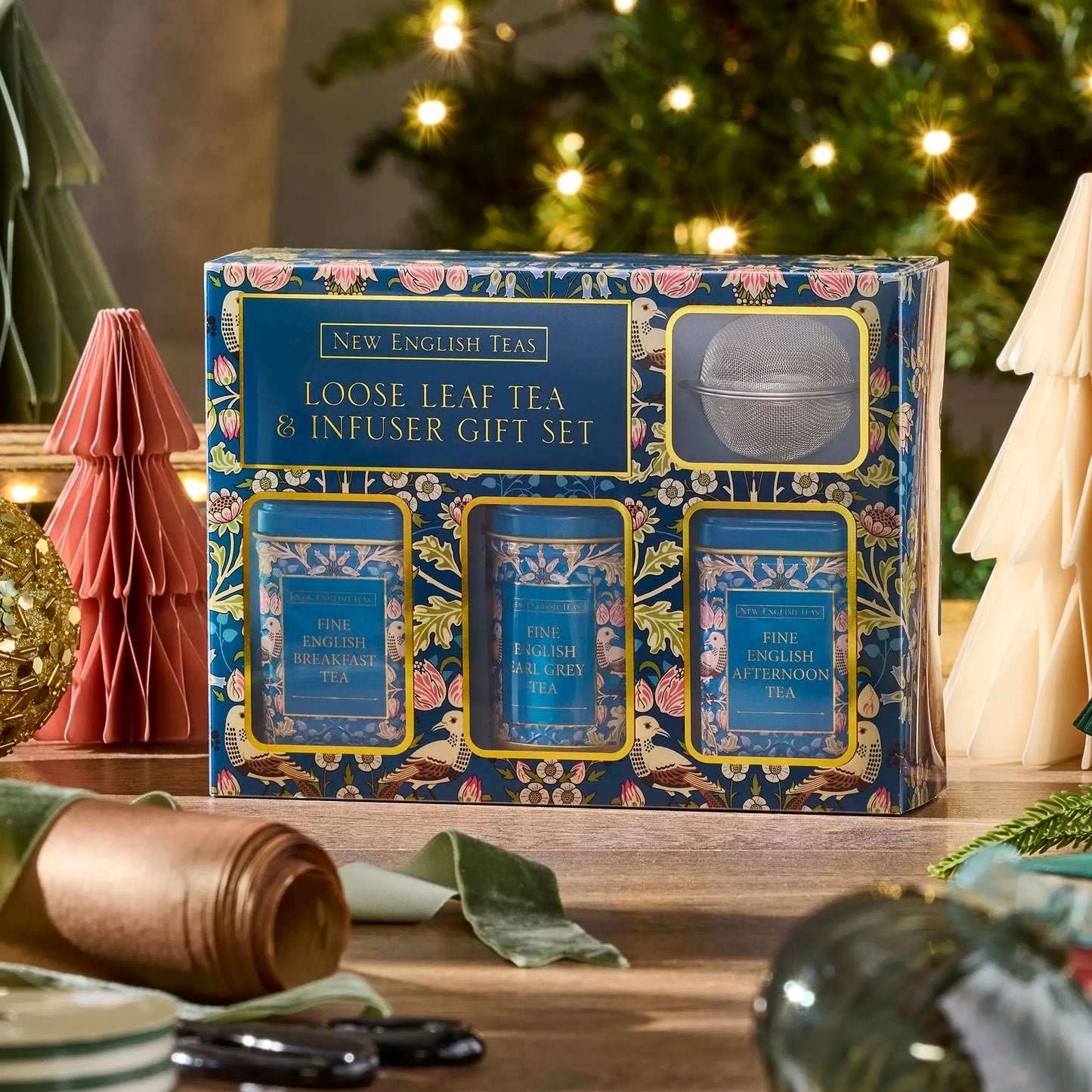 Loose leaf tea and infuser gift set with festive decor on a wooden surface. Teal design with William Morris-esque patterns.