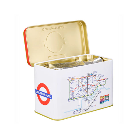 A London Underground-themed square tin container with the lid open, showing silver foil tea bags inside. The white tin features the red and blue Underground roundel logo and a multicolored transit map print on the front, with a gold interior and red rim.