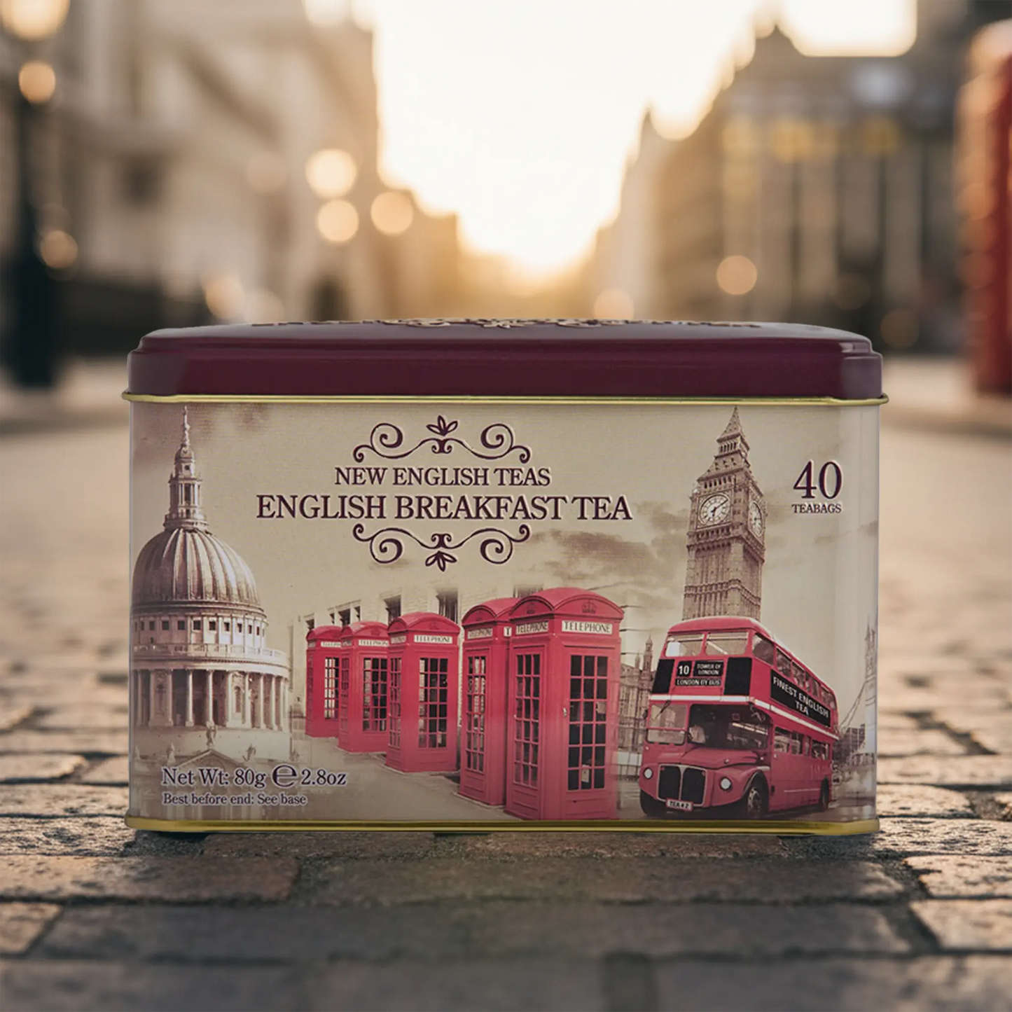 Tea tin with London-themed design featuring Big Ben, red telephone boxes, and a double-decker bus on a blurred street background.