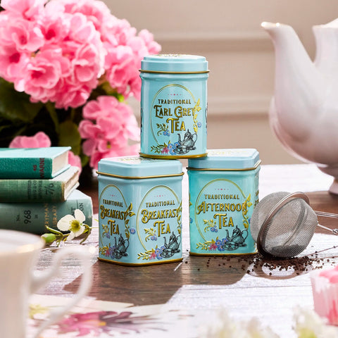 Three tea tins labeled 'Traditional Earl Grey Tea', 'Traditional Breakfast Tea', and 'Traditional Afternoon Tea' on a table with flowers and a teapot.